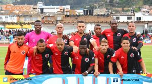 Grupo de hombres con uniformes rojos y negros, de pie en un campo de fútbol, listos para el juego.