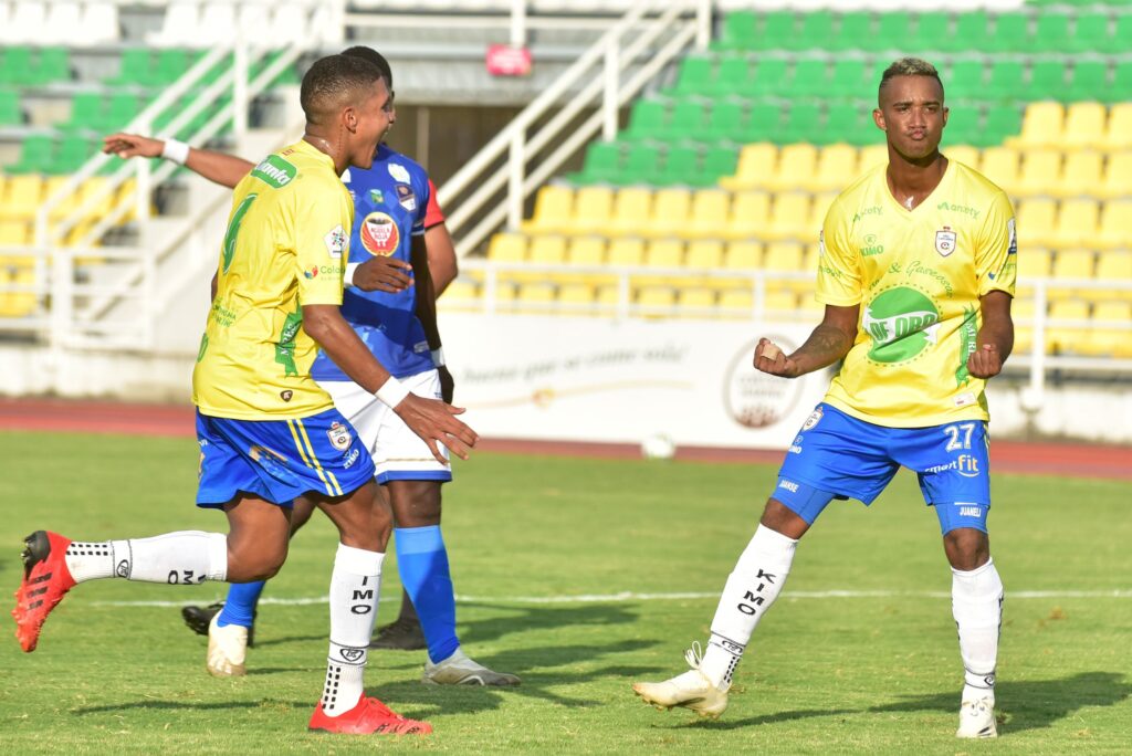 Dos hombres en uniformes de fútbol amarillos y azules compiten en el campo de juego.