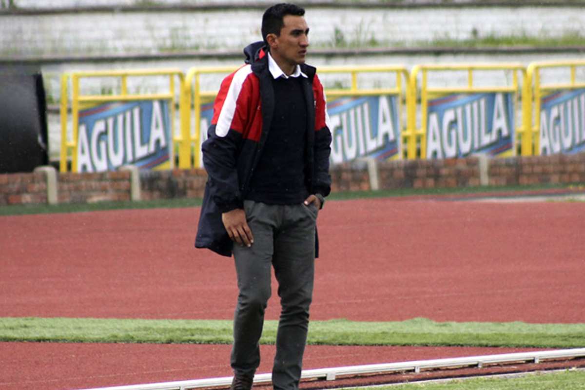 Hombre con chaqueta roja y azul de pie en un campo de fútbol